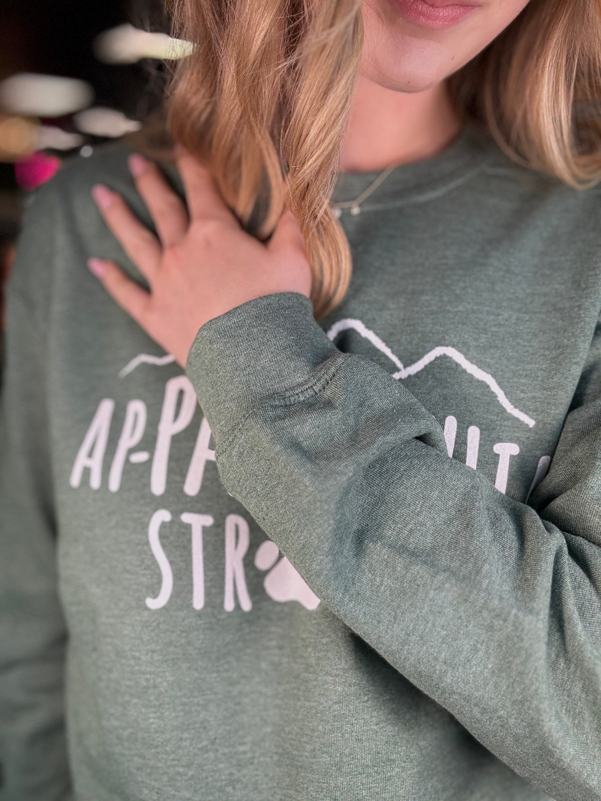 Green crewneck sweatshirt sleeve close-up with white paw and mountain graphic.