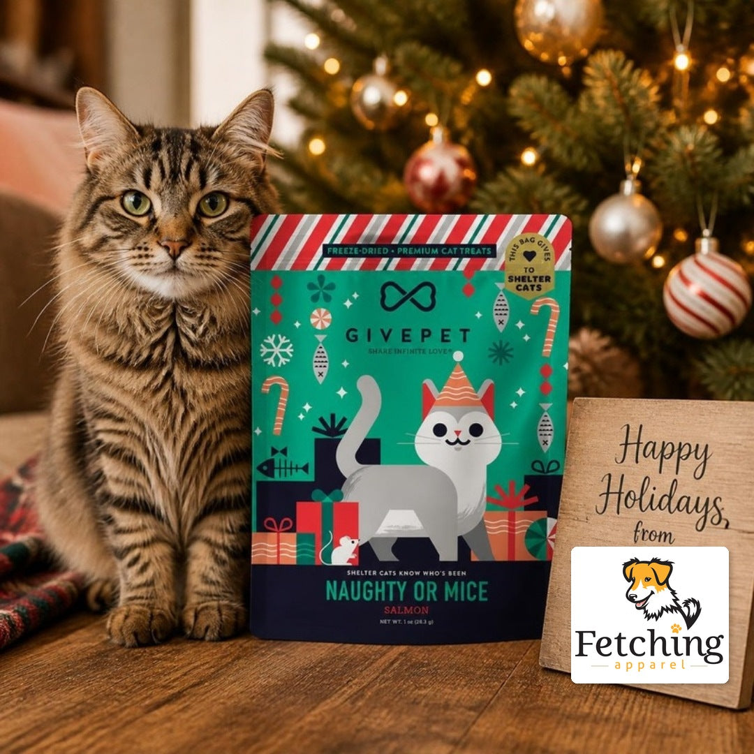 Tabby cat by a Christmas tree with a bag of Naughty or Mice freeze-dried salmon cat treats and a Happy Holidays sign with the Fetching Apparel logo